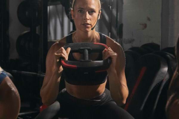 A female les mills instructor doing squat with a les mills weight plate on hand